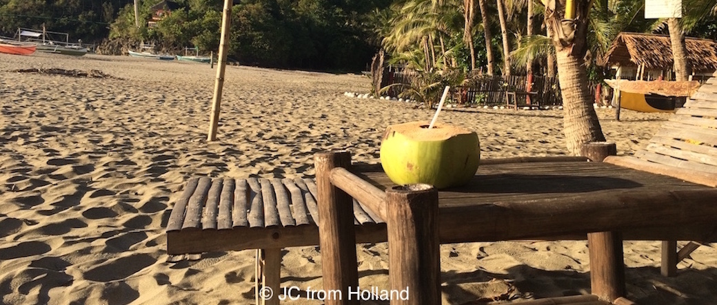 kokosnoot met rietje op bamboe tafeltje op het strand in de avondzon
