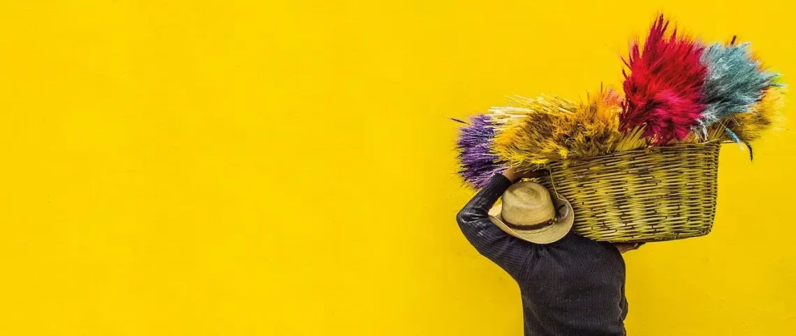 gele muur met op de voorgrond man met mand met kleurrijke materialen gezien op zijn rug.