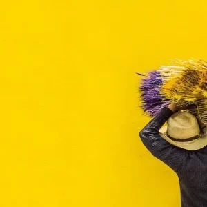 gele muur met op de voorgrond man met mand met kleurrijke materialen gezien op zijn rug.